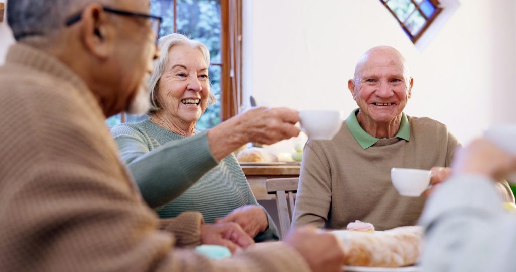 Toast, tea party and a group of elderly people in the living room of a community home for a social.